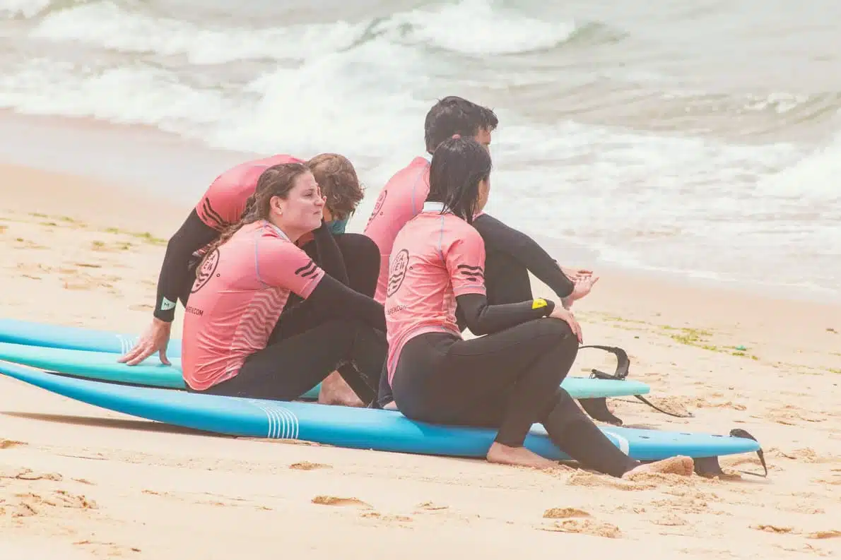 Sea Krew surf students in branded pink rashguards practicing pop-up technique on Ericeira beach