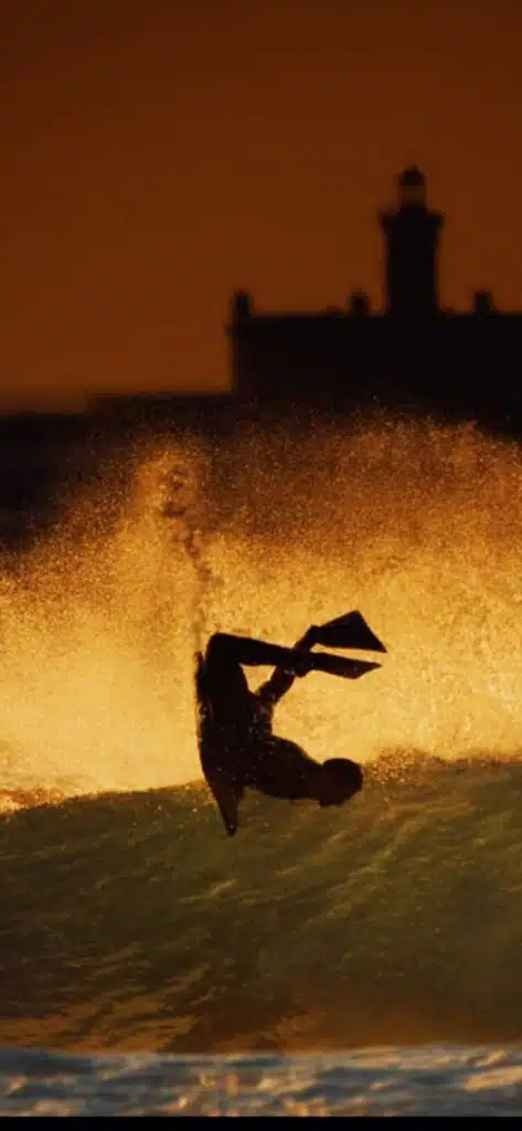 Bodyboard air silhouetted at sunset in front of a lighthouse