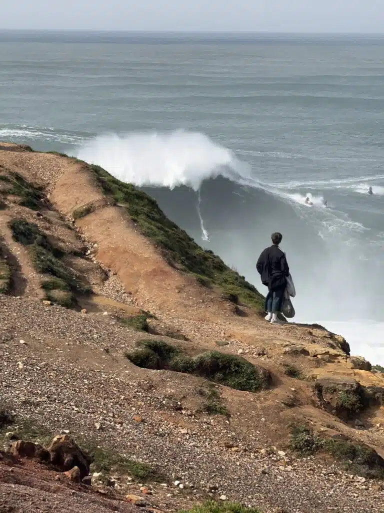 Big wave breaking below the cliff at Nazaré with a jet ski and surfer