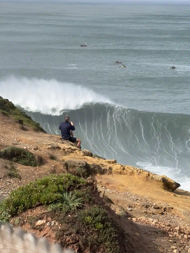 Spotter on the cliff watching a giant wave break at Praia do Norte, Nazaré