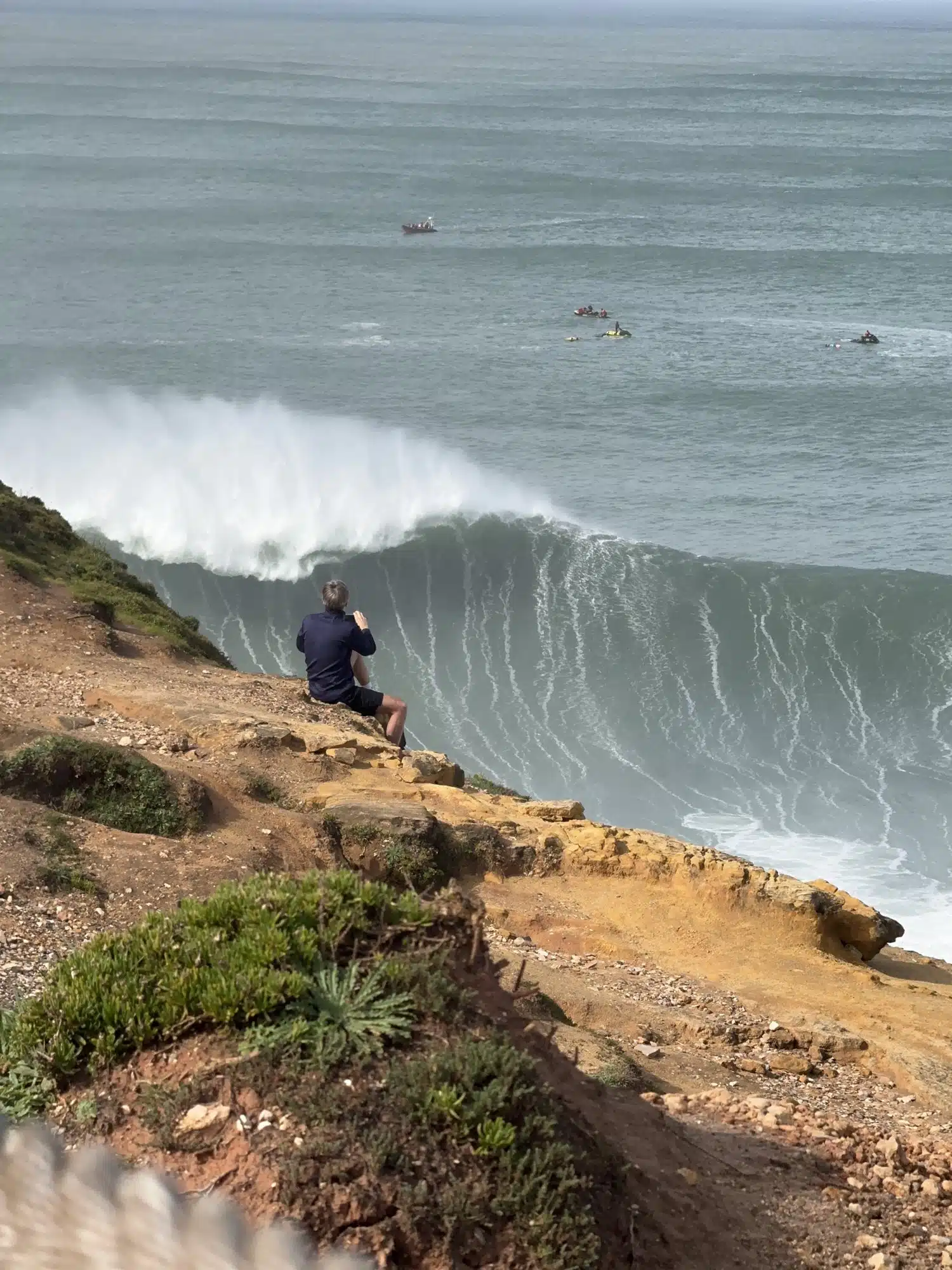 Spotter on the cliff watching a giant wave break at Praia do Norte, Nazaré