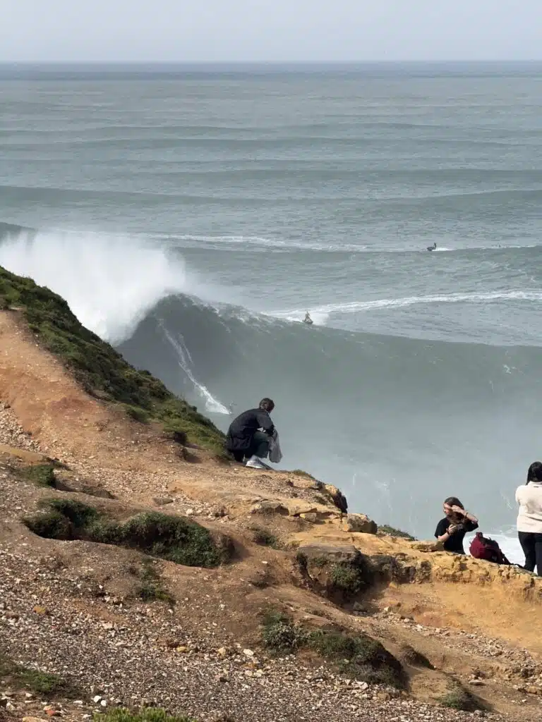 Tow surfer riding a big wave at Nazaré seen from the cliff